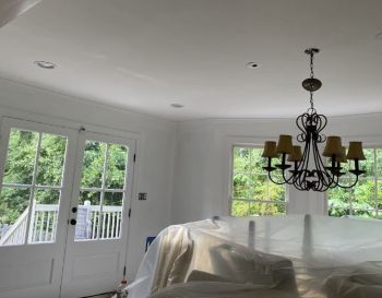 Freshly painted room with covered furniture, chandelier, and large windows overlooking a deck